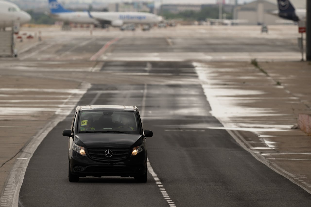 A black van driving on a rainy airport runway in Madrid, Spain, with planes visible in the background.